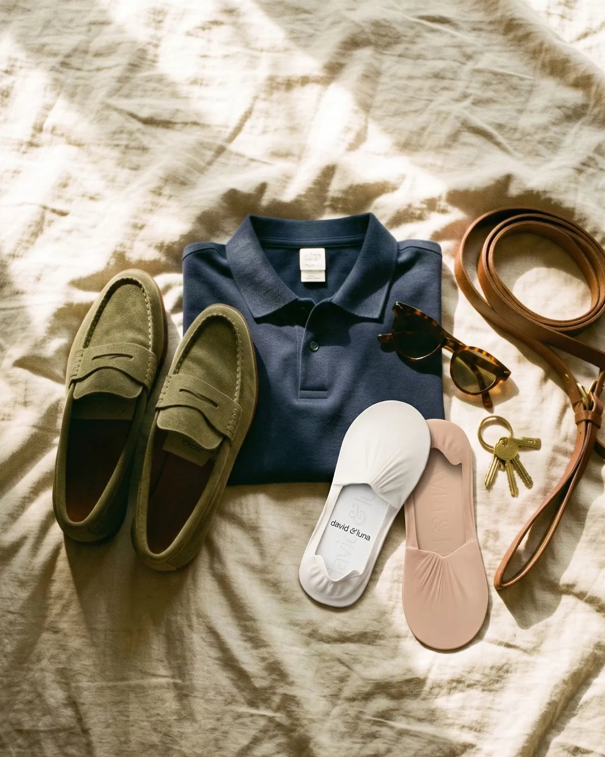 A folded navy polo with olive suede loafers and no-show socks laid out on linen